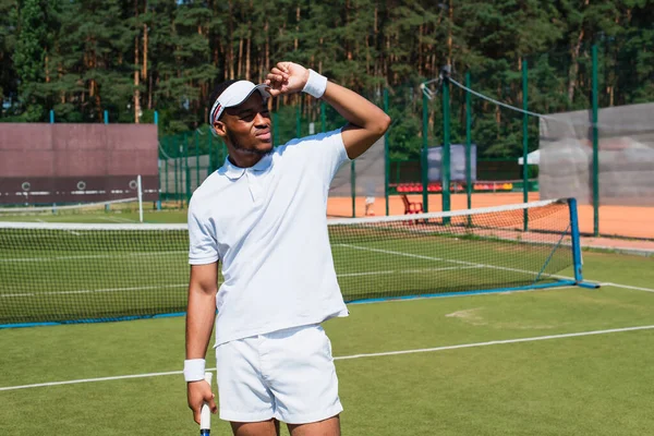 Jugador de tenis afroamericano sosteniendo raqueta y mirando hacia otro lado en la cancha - foto de stock