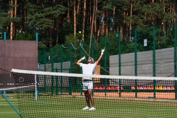 Excited african american sportsman looking at ball near net on tennis court — Stock Photo