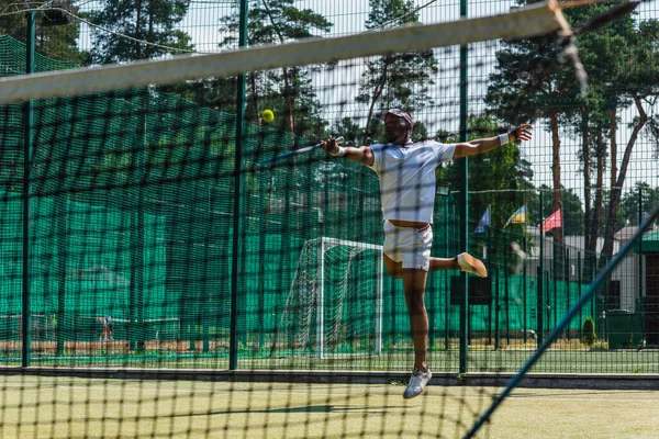 African american sportsman jumping while playing tennis near net — Stock Photo