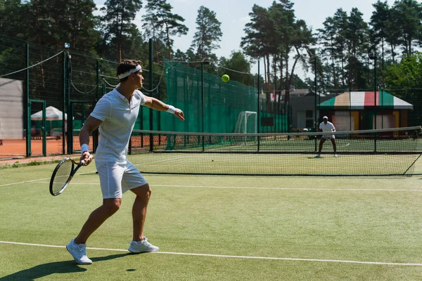 Young sportsman playing tennis with blurred african american friend on court — Stock Photo