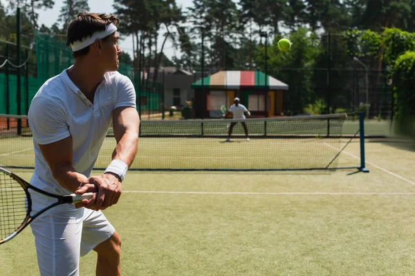 Esportista com raquete jogando tênis com amigo afro-americano desfocado ao ar livre — Fotografia de Stock