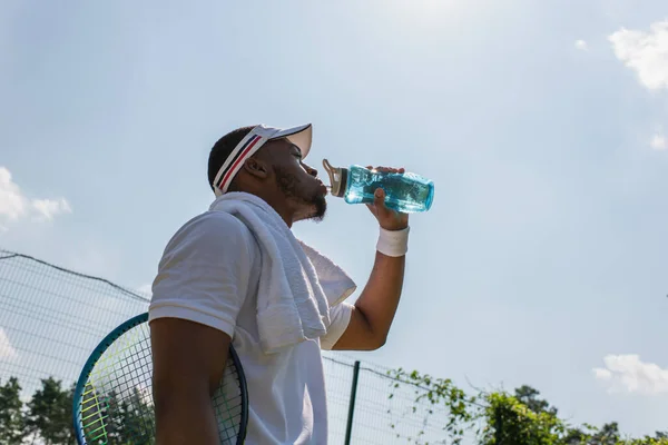 Vista de bajo ángulo del jugador de tenis afroamericano bebiendo agua en la cancha - foto de stock