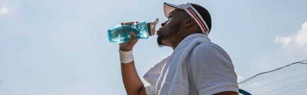 Visão de baixo ângulo do esportista afro-americano bebendo água ao ar livre, bandeira — Fotografia de Stock