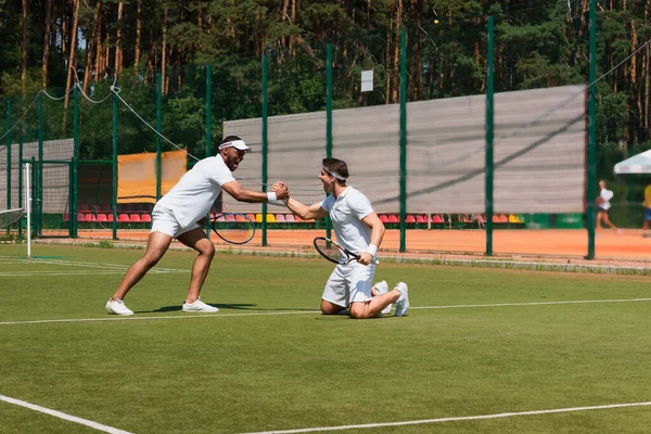 Excited multiethnic tennis players shaking hands on court — Stock Photo