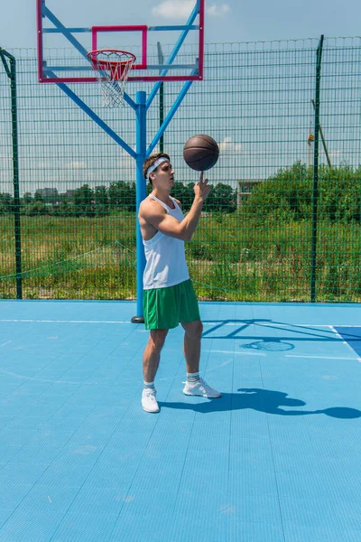 Jovem desportista girando bola de basquete no dedo no playground — Fotografia de Stock