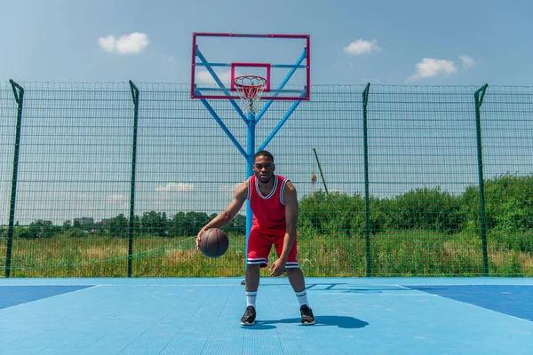 Afro-américain homme regardant caméra tout en jouant streetball sur aire de jeux — Photo de stock