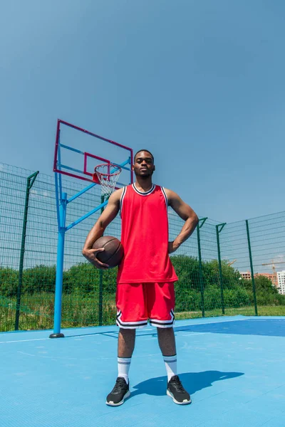 Sportivo afroamericano che tiene palla da basket e mano sull'anca nel parco giochi — Foto stock