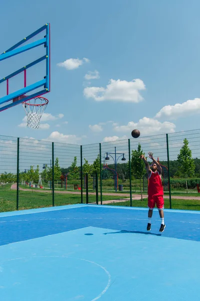 Un sportif afro-américain sautant et lançant un ballon de basket dans un cerceau — Photo de stock