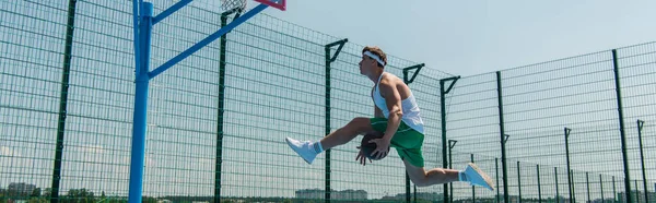 Side view of young sportsman with basketball ball jumping near hoop, banner — Stock Photo