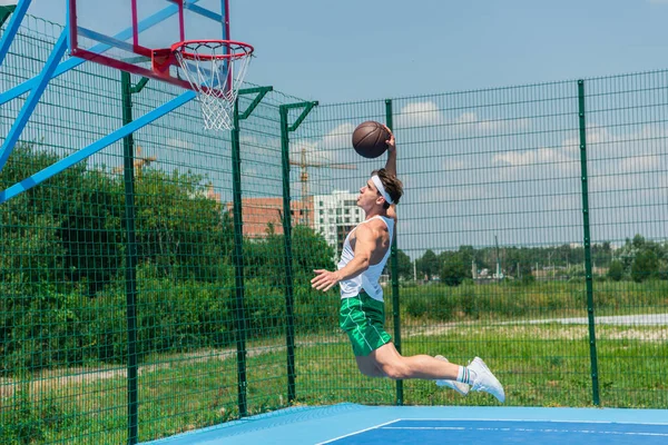 Vista lateral del deportista saltando bajo el aro mientras juega streetball - foto de stock