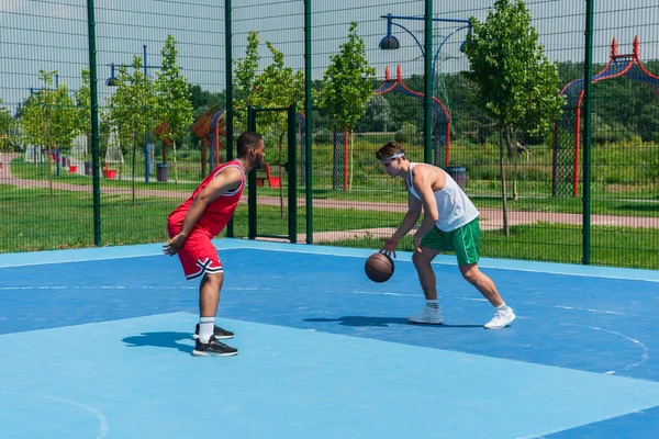 Des joueurs de streetball multiethniques s'entraînent avec un ballon de basket sur une aire de jeux — Photo de stock