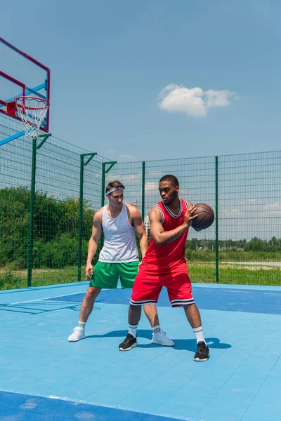 Giocatore di streetball afroamericano che tiene la palla vicino ad un amico nel parco giochi — Foto stock