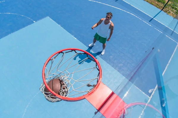Top view of basketball ball in hoop near blurred sportsman on playground — Stock Photo