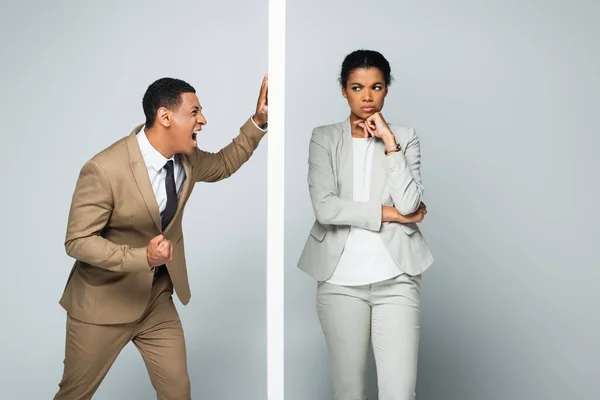 Angry african american businessman screaming near wall and pensive businesswoman on grey — Stock Photo