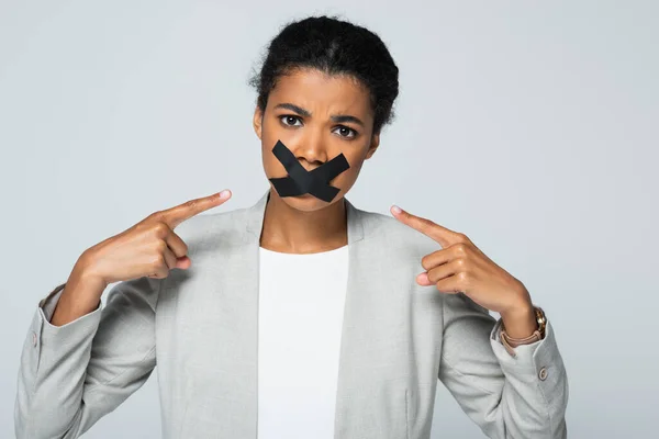 Afro-américaine femme d'affaires pointant sur scotch tape sur la bouche isolé sur gris — Photo de stock