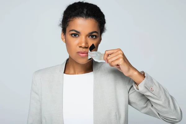 Mujer de negocios afroamericana despegando cinta adhesiva en boca aislada en gris - foto de stock