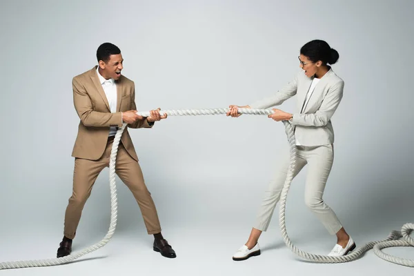 Empresario y mujer de negocios tirando de la cuerda en gris, concepto de igualdad de género - foto de stock