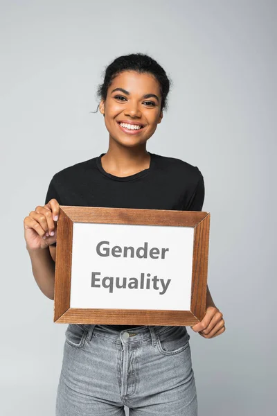Щаслива афроамериканська жінка тримає плакат з написом гендерної рівності ізольовано на сірому — стокове фото