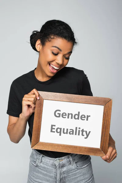 Здивована афроамериканська жінка тримає плакат з гендерною рівністю ізольовано на сірому — стокове фото