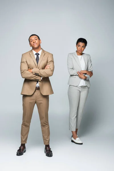 Full length of arrogant african american businessman with crossed arms near upset woman on grey — Stock Photo