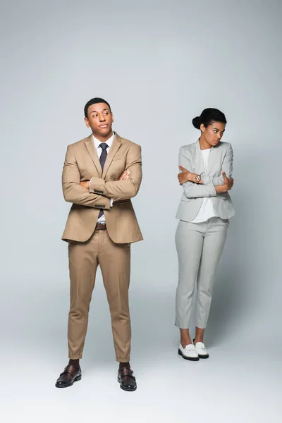 Full length of arrogant businessman with crossed arms near upset african american woman on grey — Stock Photo