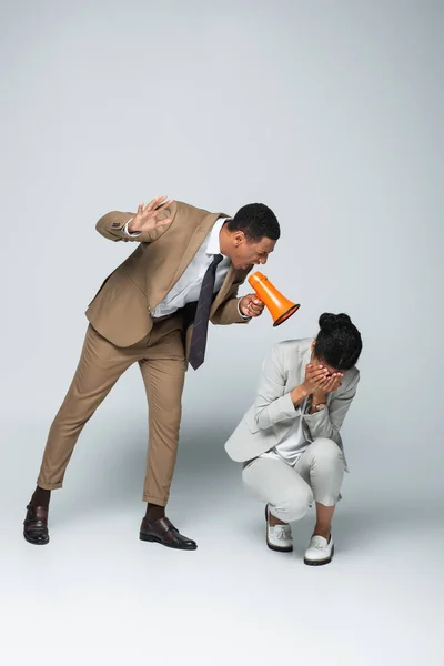Angry african american businessman screaming at scared businesswoman while holding megaphone on grey — Stock Photo