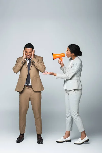 Angry african american businesswoman screaming at scared businessman while holding megaphone on grey — Stock Photo