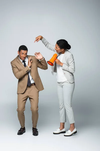 Arrabbiato afro-americano donna d'affari urlando e indicando uomo d'affari spaventato mentre tiene megafono su grigio — Foto stock