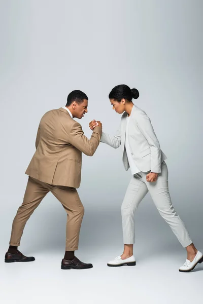 Vista lateral de la mujer de negocios afroamericana y el hombre haciendo lucha libre de brazos en gris - foto de stock