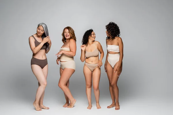 Smiling interracial women in lingerie standing on grey background, body positive concept — Stock Photo