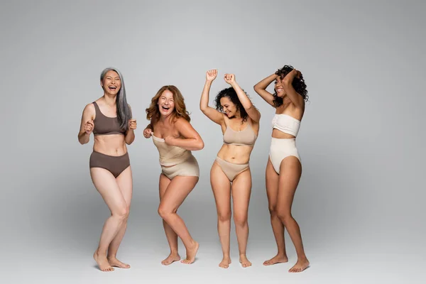 Mujeres interracial positivas en ropa interior sobre fondo gris - foto de stock