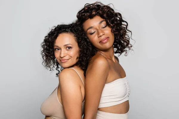 Young african american woman in lingerie standing back to back with friend isolated on grey — Stock Photo