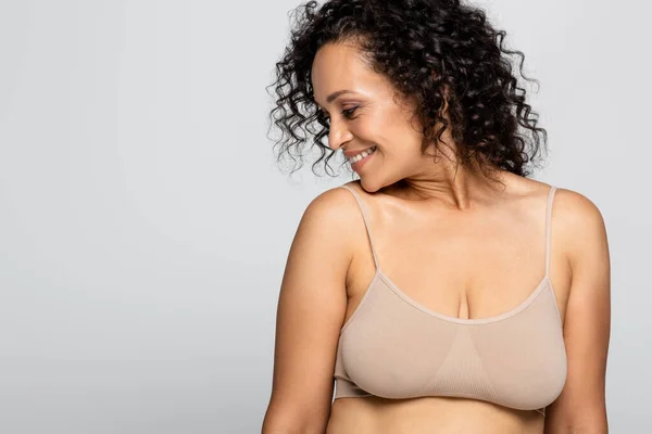 Vista lateral de la sonriente mujer afroamericana en sujetador aislado en gris, concepto positivo para el cuerpo - foto de stock