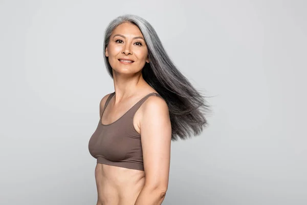 Femme asiatique en soutien-gorge souriant à la caméra isolé sur gris, corps concept positif — Photo de stock