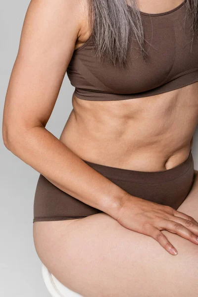 Vista ritagliata della donna in lingerie seduta sulla sedia isolata sul grigio, concetto positivo per il corpo — Foto stock