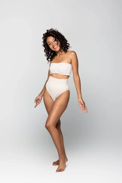 Happy barefoot african american woman in lingerie standing on grey background, body positive concept — Stock Photo