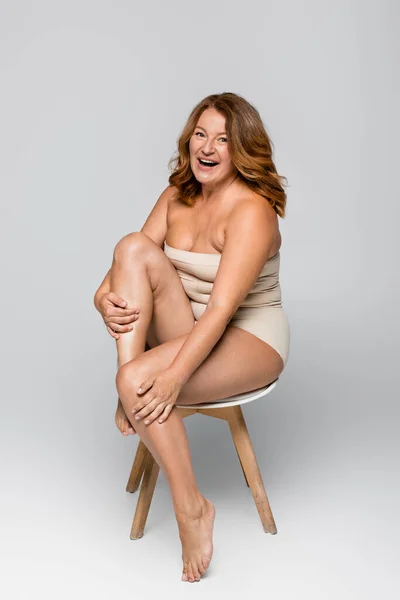Весела жінка з надмірною вагою на стільці на сірому фоні — стокове фото