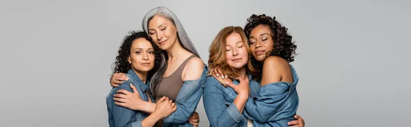 Donne multietniche in camicie di denim che si abbracciano isolate sul grigio, striscione — Foto stock