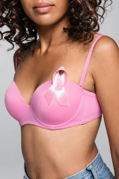 Розбитий погляд на афро-американську жінку з стрічкою обізнаності про рак молочної залози на рожевий бюстгальтер ізольований на сірому — стокове фото