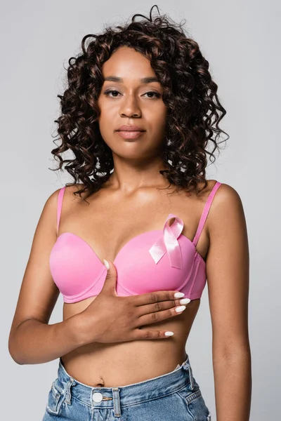 Young african american woman with pink ribbon on bra looking at camera isolated on grey — Stock Photo