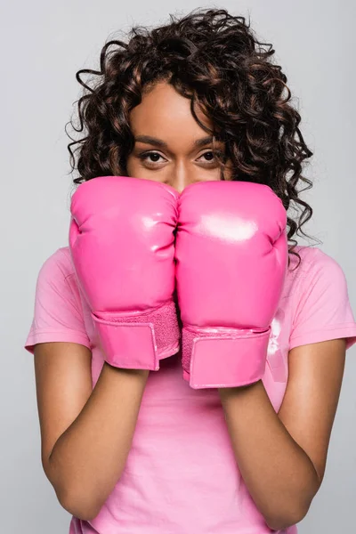 Femme afro-américaine avec ruban rose et gants de boxe regardant la caméra isolée sur gris — Photo de stock