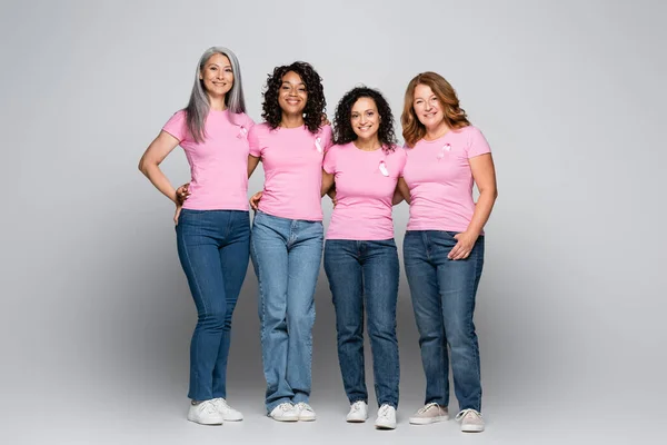 Mujeres interraciales sonrientes con cintas de conciencia sobre el cáncer de mama en un fondo gris - foto de stock