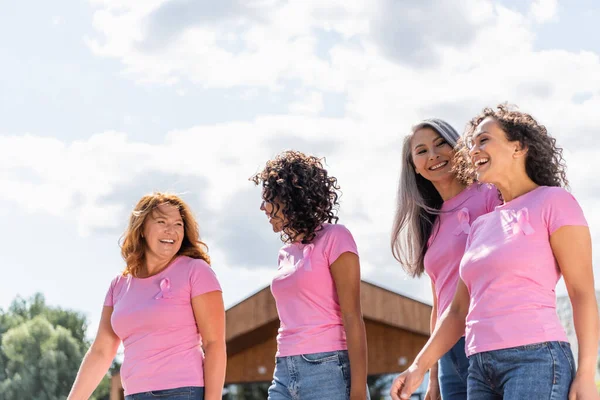 Mujeres alegres multiétnicas con cintas rosas caminando al aire libre - foto de stock