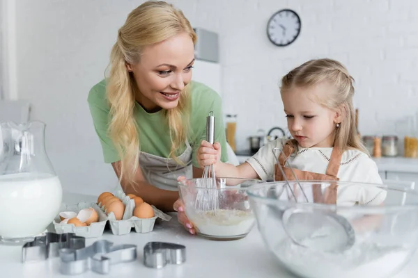 Fille mélangeant des ingrédients dans un bol tout en cuisinant avec maman dans la cuisine — Photo de stock