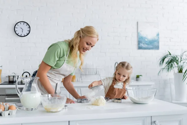 Kleines Mädchen sichtet Mehl, während es Mutter in der Küche hilft — Stockfoto