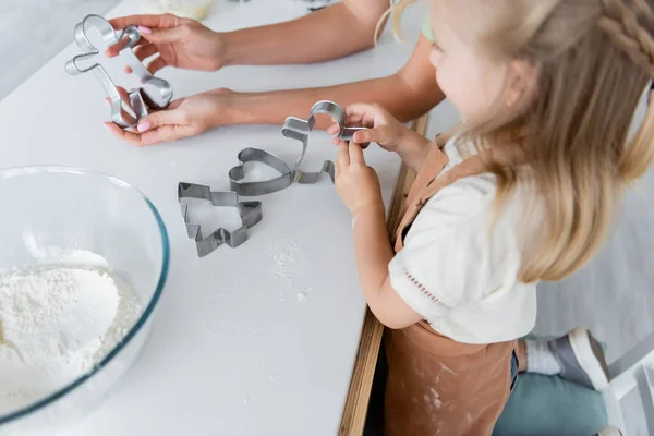 Woman showing cookie cutter to blurred daughter in kitchen — Stock Photo