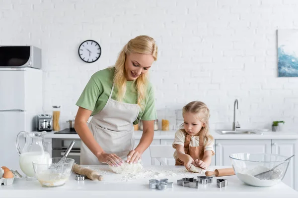 Mãe e filha em aventais amassar massa de farinha na cozinha — Fotografia de Stock
