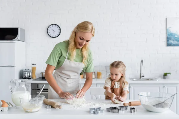 Mère et fille dans des tabliers pétrissant la pâte dans la cuisine — Photo de stock