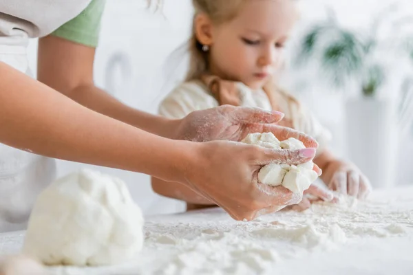 Женщина месит тесто возле размытой дочери на кухне — стоковое фото