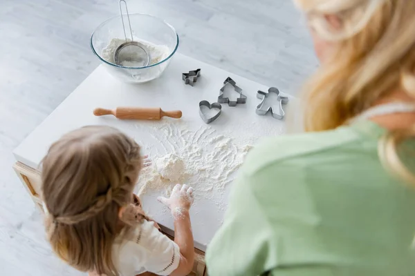 Vue aérienne de la fille pétrissant la pâte près de maman floue dans la cuisine — Photo de stock